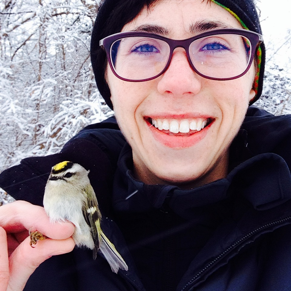 Leah, holding a Golden-crowned Kinglet, smiles at the camera.